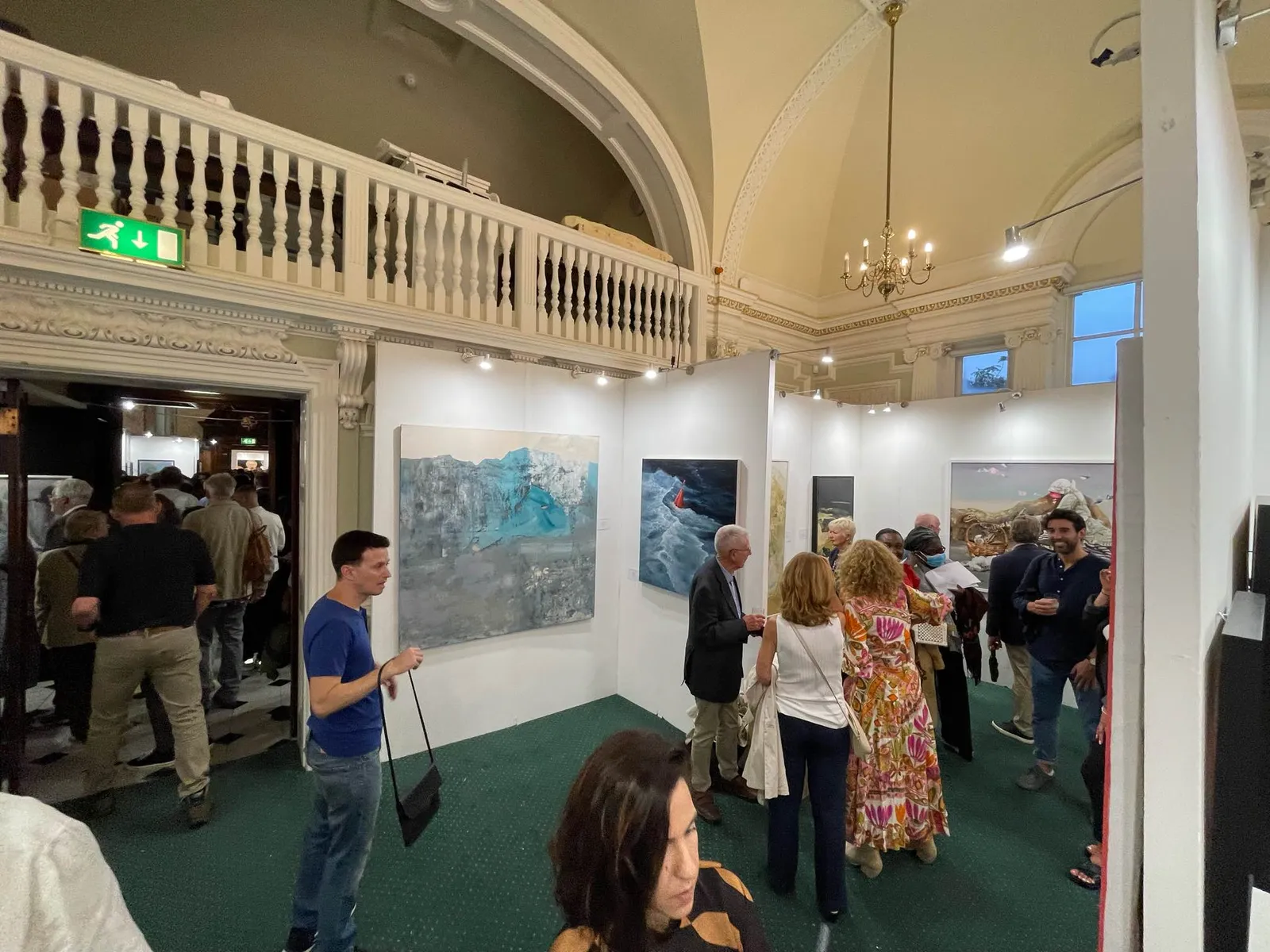 Vizitatori și artiști adunați sub tavanul boltit de la Chelsea Old Town Hall, la vernisajul London Art Biennale 2023