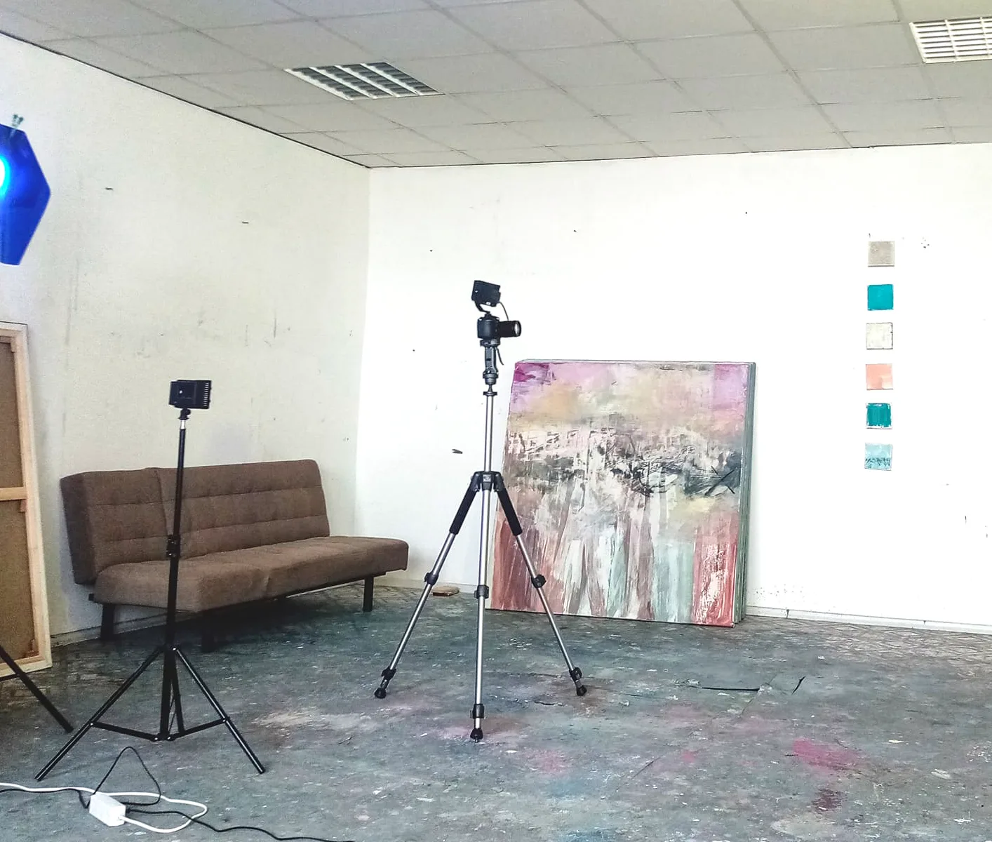 Studio documentation setup with two camera tripods and portable lights positioned in front of an abstract painting, showing the process behind photographing a work for the digital archive
