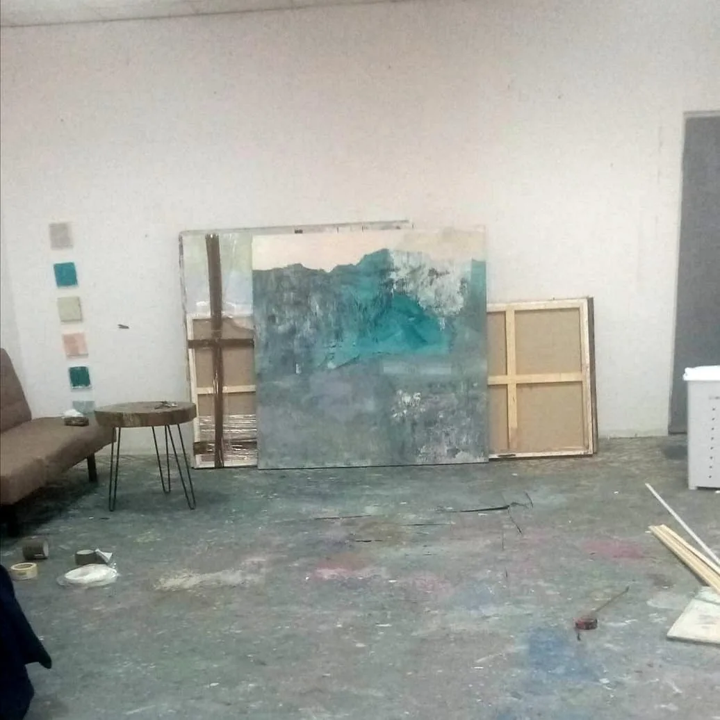 Unfinished paintings from Adrian Dică's studio leaning against a wall next to a small side table, still surrounded by tape and materials before being catalogued into the archive